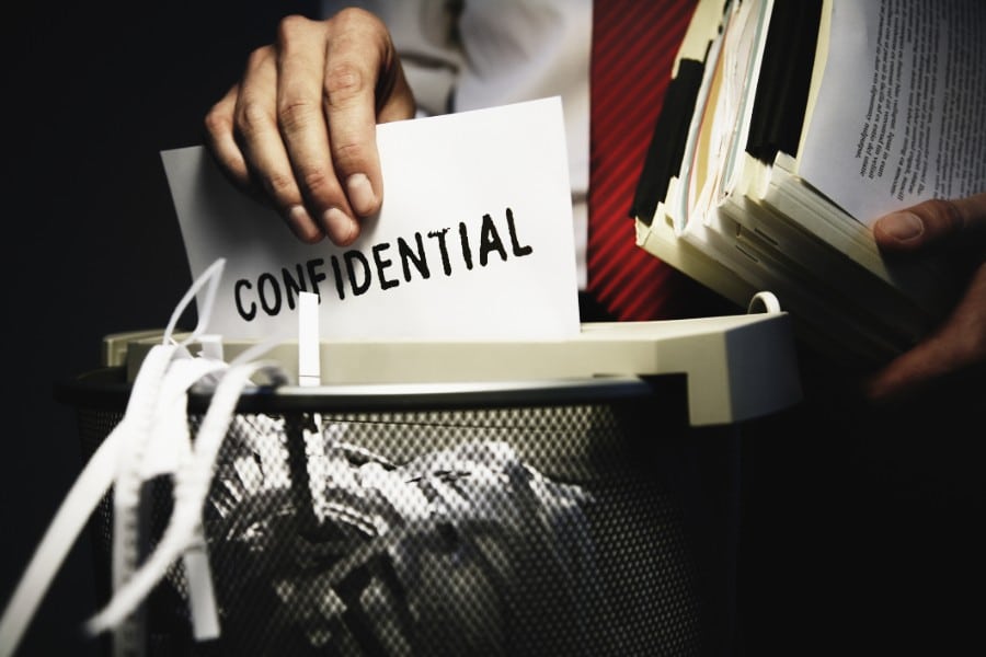 A lawyer puts a paper marked confidential into a shredder to protect client data